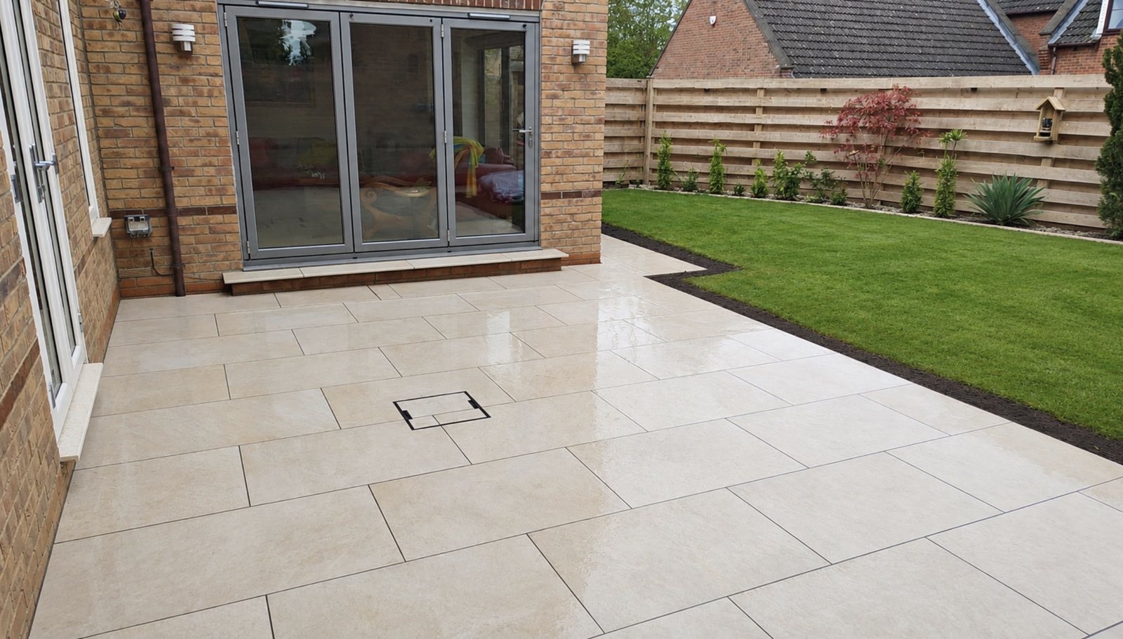 Light large-format porcelain patio outside grey bifold doors with a lawn beyond in Stamford Light large-format porcelain patio outside grey bifold doors with a lawn beyond in Stamford